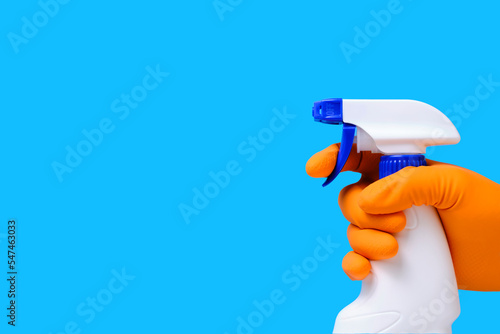 Sprayer for cleaning windows and plumbing in hand with glove on blue background.