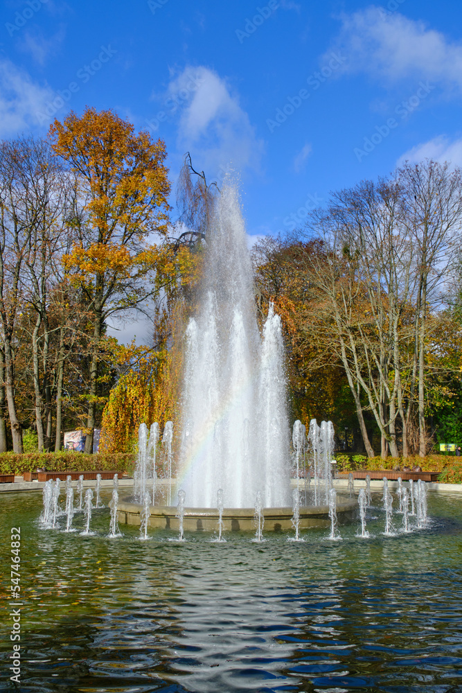 Beautiful fountain with blue sky and trees with yellowed autumn foliage.