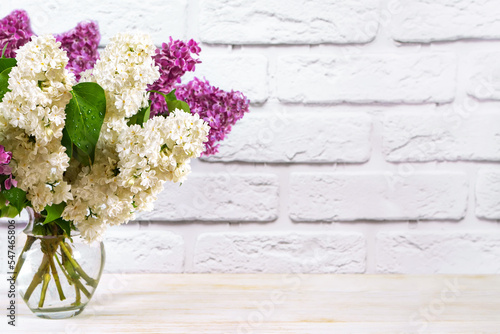 Beautiful blooming purple and white lilac flowers in vase on white wall brick background. Floral composition. Women day, mother day, birthday and wedding concept. Mockup, copy space for text