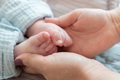 Close-up of a mother's hands cradling the feet of her newborn Caucasian child. The impact of demographic changes, birth rate and mortality