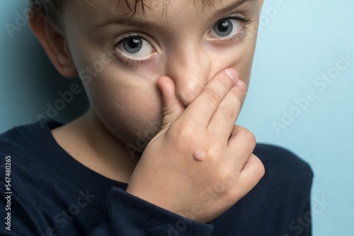 a boy of European appearance covers his mouth with his hand. papilloma in a child close-up