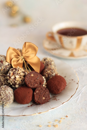 Chocolate truffles coated in a sprinkling of walnuts and cocoa on a white plate with a gold stripe, decorated with a gold bow on a white background, a warm Christmas atmosphere, xmas decorations.