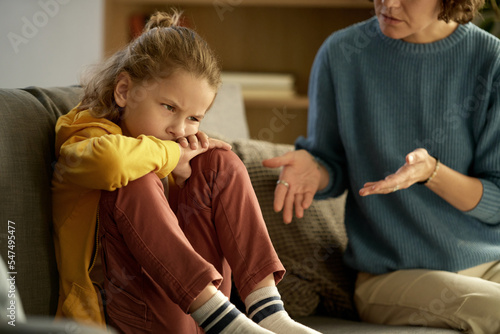 Fotografie Naughty child sitting on couch with dissatisfied expression on his face while mo