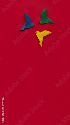 three paper origami pigeons yellow  green and blue on red background  vertical  16 9  copy space