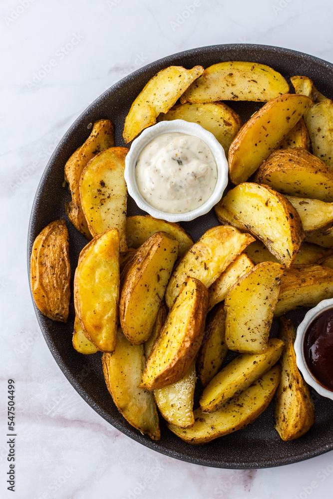 Oven roasted potatoes with skins, sliced, with sauces close-up, top view Oven roasted potatoes with skins, sliced, with sauces close-up, top view