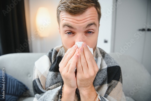 Sick man on sofa at home and blowing nose