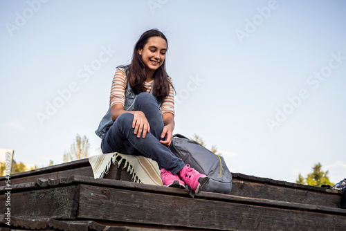 Portrait of a teenage girl student with a backpack sitting in a university park on an autumn day