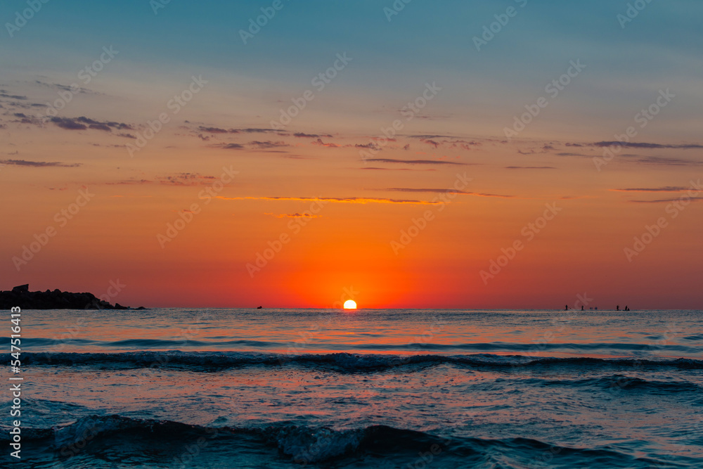 Beautiful sunrise landscape seen from the beach, the sun rising from the sea horizon and painting the sea in orange and blue colors