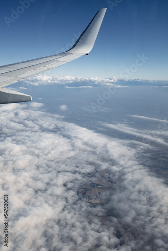 Flying above the white clouds on a beautiful landscape sky from an airplane window with the wing in the frame