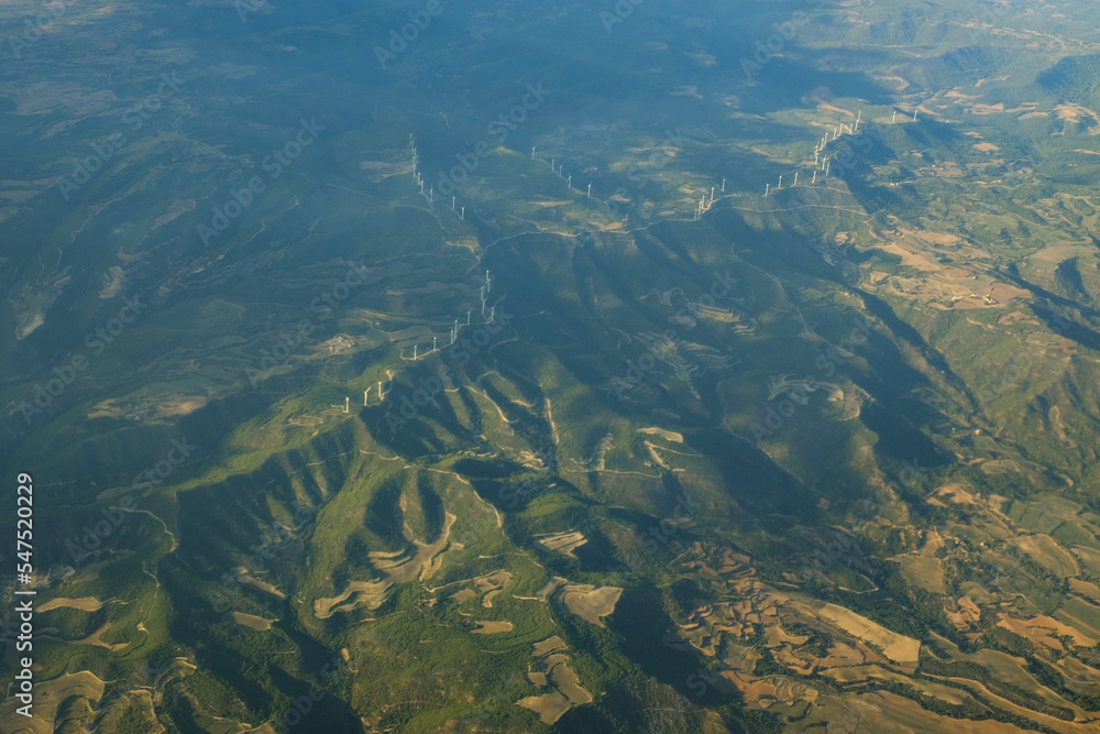 White wind mills in a row on a top of a mountain green landscape in Spain, seen from an airplane