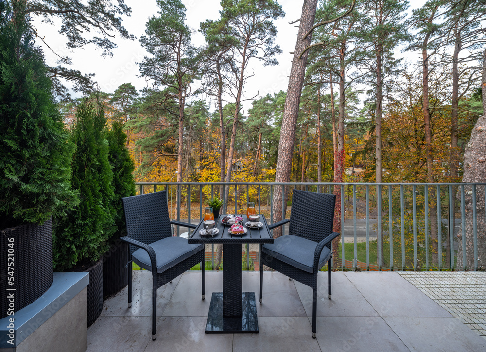 Cozy balcony terrace of luxury private house. Cottage near autumn forest. Grey table and chairs. Drinks and sweets.