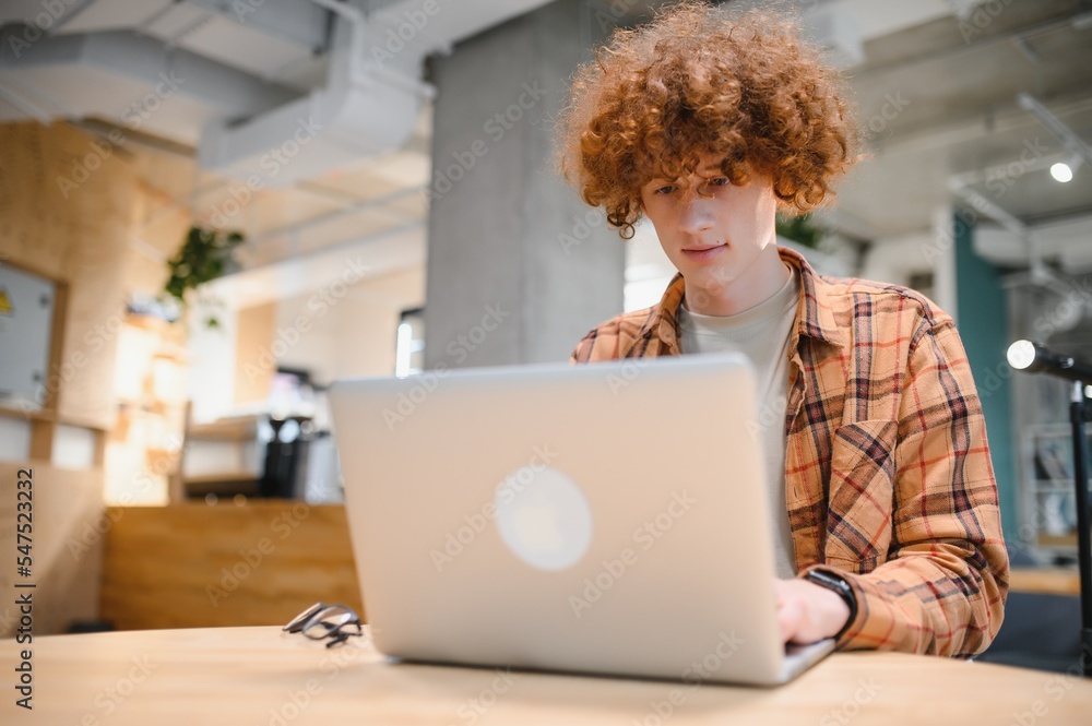 Young happy male freelancer in casual clothes sitting in cafe with laptop and using mobile phone. Young happy male freelancer in casual clothes sitting in cafe with laptop and using mobile phone.