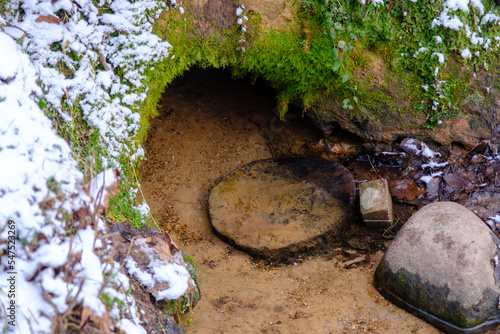 The water flows from a small cave opening, forming a natural spring. Skanaiskalns nature park. November is the first snow in Mazsalaca in Latvia photo
