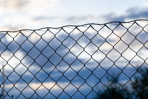 blue beautiful light sky where on one side there are dark blue gray clouds and below them you can see the dark silhouette of a metal fence