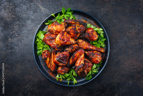 Traditional barbecue chicken wings and drumsticks with hot chili and coriander served as top view on a rustic plate with copy space