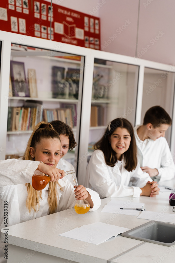 School education. Cheerful classmates in chemistry lesson hold flasks with liquid for experiments. Happy friends study together in class in laboratory. School education. Cheerful classmates in chemistry lesson hold flasks with liquid for experiments. Happy friends study together in class in laboratory.