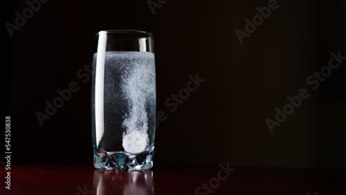 A soluble tablet for colds, treatment. Throw an effervescent tablet into a glass of water, dark background, night apartment interior photo