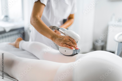 Leg endermology LPG performed by unrecognizable caucasian specialist in white uniform on her Asian client. Protective gear and clothing. Beauty salon interior. High quality photo photo