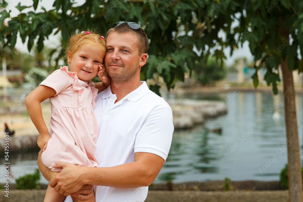 Dad holds his daughter in his arms, a walk in the city park, family leisure Dad holds his daughter in his arms, a walk in the city park, family leisure