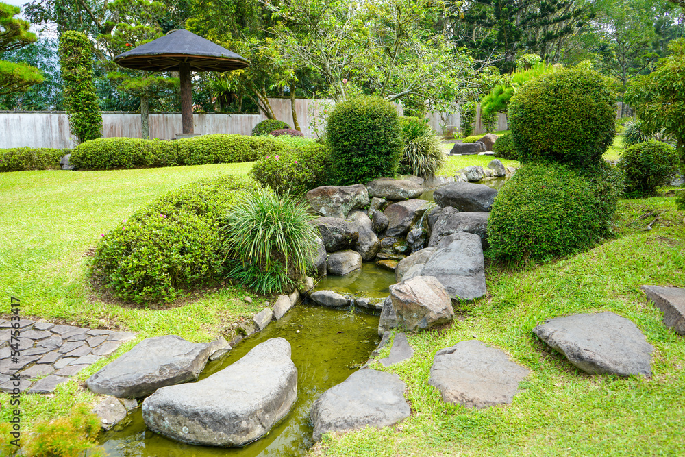 Traditional oriental park or garden from Japan or China with fish pond, lake or river, wooden bridge, meadow, and trees. Japanese garden design. Taman Bunga Nusantara, Cianjur, West Java, Indonesia. Traditional oriental park or garden from Japan or China with fish pond, lake or river, wooden bridge, meadow, and trees. Japanese garden design. Taman Bunga Nusantara, Cianjur, West Java, Indonesia.
