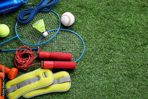 Set of different colorful sports equipment on green grass, above view. Space for text