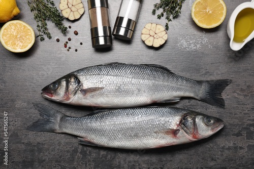 Fresh raw sea bass fish, seasonings and lemons on black table, flat lay photo