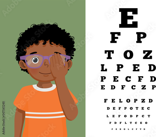 Cute little African boy with eyeglasses cover his eye having vision test reading block letters at ophthalmologist office