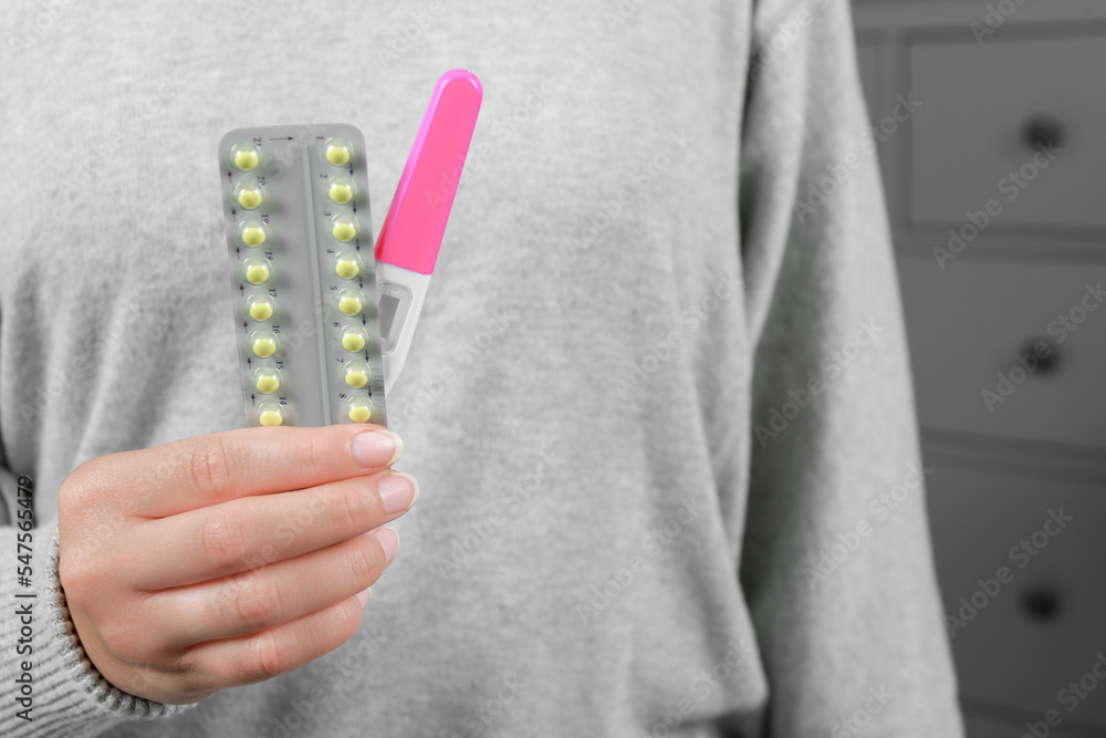Woman holding birth control pills and pregnancy test indoors, closeup