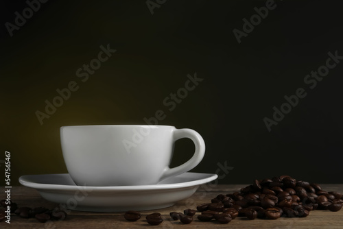 Cup of hot aromatic coffee and roasted beans on wooden table against dark background