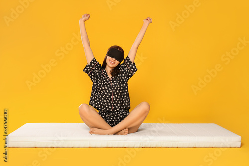 Woman in sleep mask stretching on soft mattress against orange background