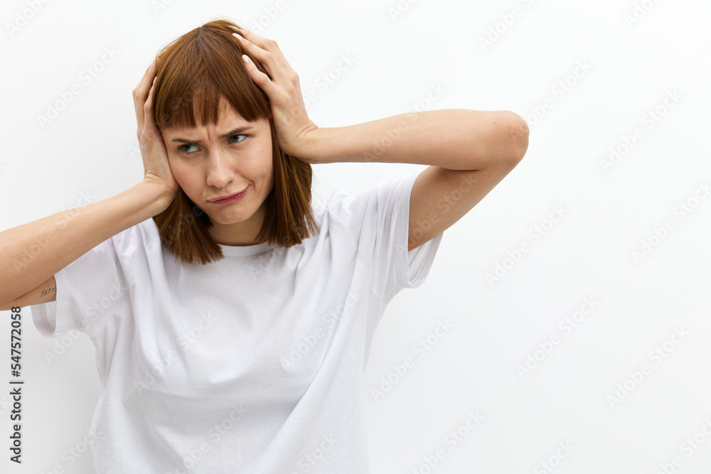 a funny, emotional woman stands on a light background in a T-shirt and holds her head with her hands while expressing emotions. Horizontal photo with an empty space for inserting an advertising layout a funny, emotional woman stands on a light background in a T-shirt and holds her head with her hands while expressing emotions. Horizontal photo with an empty space for inserting an advertising layout