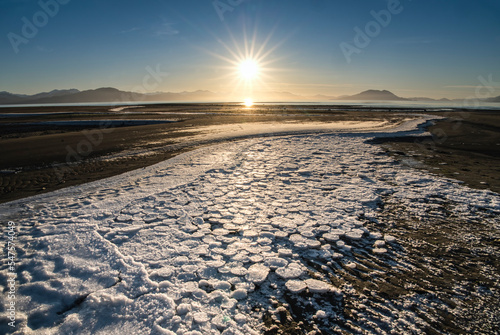 Ice circles on beach with setting sunburst in Southeast Alaska in winter.