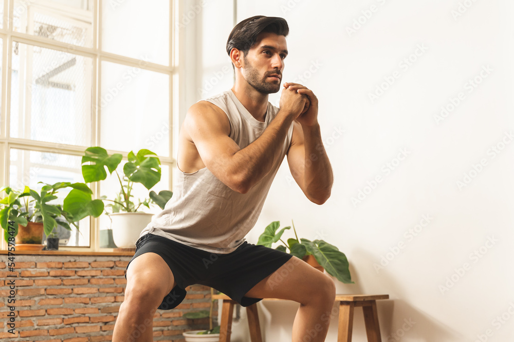 Obraz premium Handsome fitness caucasian young man, guy wearing sportswear training strength muscles workout, cardio exercise training in living room at home for healthy body strong athletic, fit active lifestyle