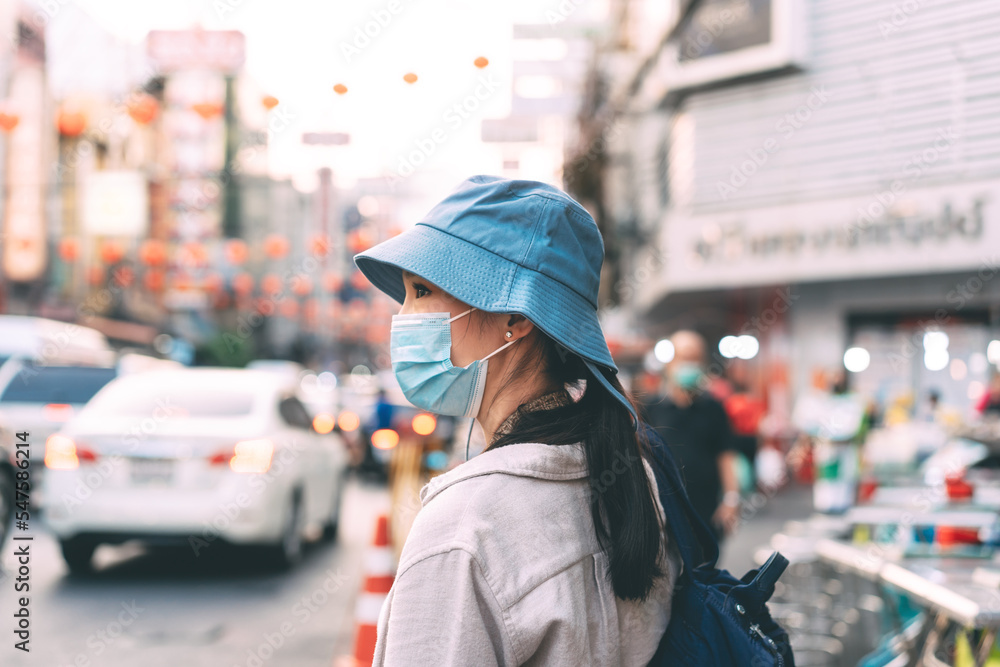 Walking young adult asian woman traveller wear face mask for covid-19 traveling in local city on summer day