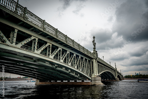 Bridge. A low metal bridge across the river in cloudy weather in gloomy dark colors. St. Petersburg © Celt Studio