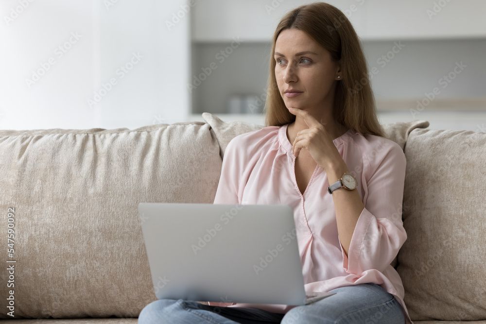 Young woman ponder answer to client working at home using laptop on weekend. 35s female choose goods and services buying on internet sit on sofa with computer looks undecided. Leisure, telework, tech Young woman ponder answer to client working at home using laptop on weekend. 35s female choose goods and services buying on internet sit on sofa with computer looks undecided. Leisure, telework, tech