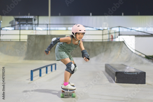 asian child skater or kid girl fun riding skateboard or surf skate with wave bank ramp and rail bars to street surfing in skatepark by extreme sports exercise to wear helmet for body safety at night