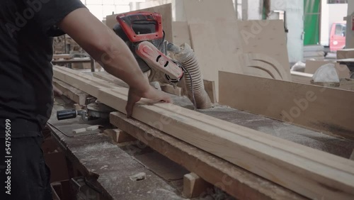 Factory worker cuts wooden bars on a circular saw. Sawdust is flying