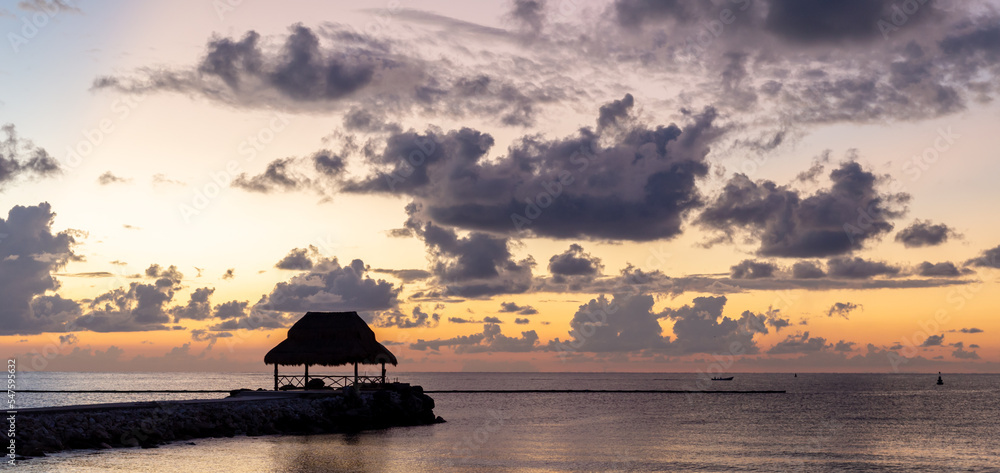 silhouette d'une cabane avec un toit de paille sur la mer lors d'un lever de soleil très coloré