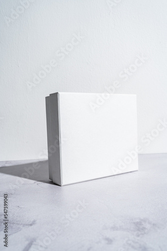 White square gift box mockup on gray concrete background. Closeup, shadows, minimalist concept