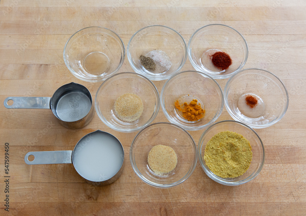 Looking down at a cup of coconut milk and various spices, such as tumeric, nutritional yeast, paprika, garlic, salt, pepper on wooden cutting board. Looking down at a cup of coconut milk and various spices, such as tumeric, nutritional yeast, paprika, garlic, salt, pepper on wooden cutting board.
