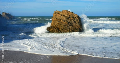 Swell breaking on the beach of Biarritz in the Basque Country with the lighthouse on the horizon (in slow motion)