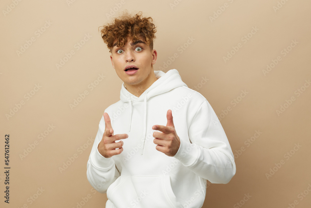 a funny, happy man stands on a beige background in a white hoodie and shows his index fingers to the camera with his mouth wide open in surprise a funny, happy man stands on a beige background in a white hoodie and shows his index fingers to the camera with his mouth wide open in surprise