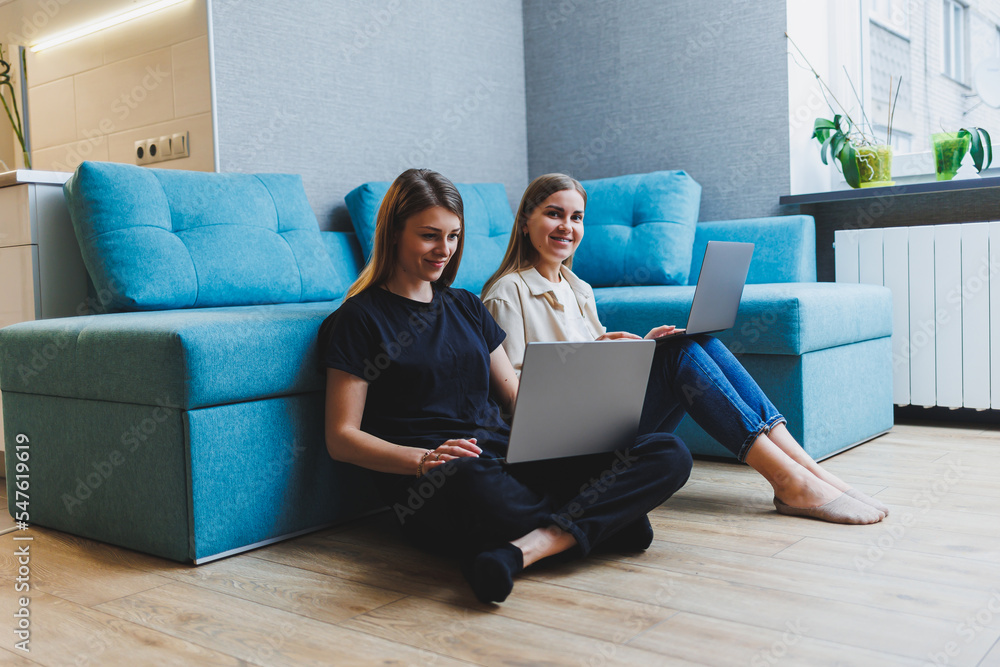 Two cute women working using laptop in living room on sofa. Friends, friendship, time together. Girlfriends are sitting on the couch and watching a movie Two cute women working using laptop in living room on sofa. Friends, friendship, time together. Girlfriends are sitting on the couch and watching a movie