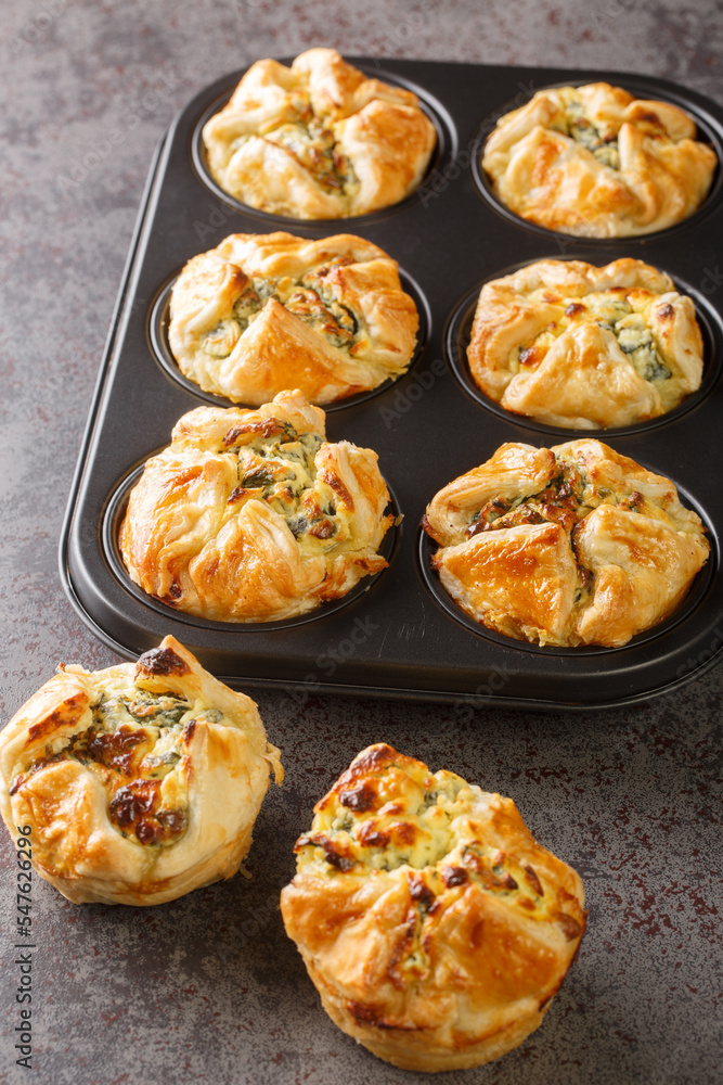 Puff pastry muffins stuffed with spinach and feta cheese close-up in a muffin pan on the table. Vertical