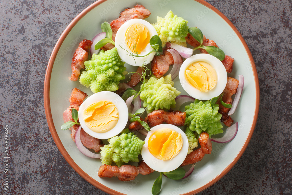 Romanesco cabbage salad with bacon, boiled eggs, red onion and microgreens closeup on the plate on the table. Horizontal top view from above Romanesco cabbage salad with bacon, boiled eggs, red onion and microgreens closeup on the plate on the table. Horizontal top view from above