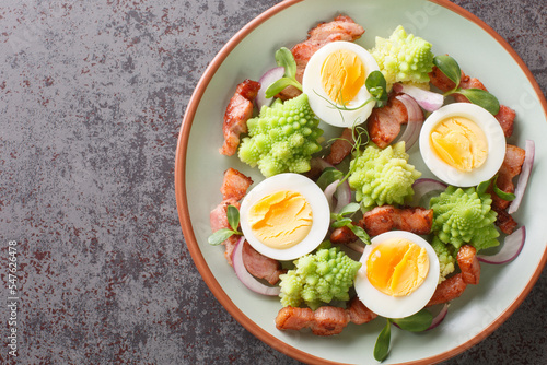 Steamed romanesco broccoli, boiled eggs, fried bacon and fresh microgreens close-up in a plate on the table. Horizontal top view from above