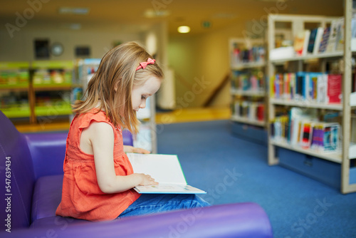 Preschooler old girl reading a book in municipal library