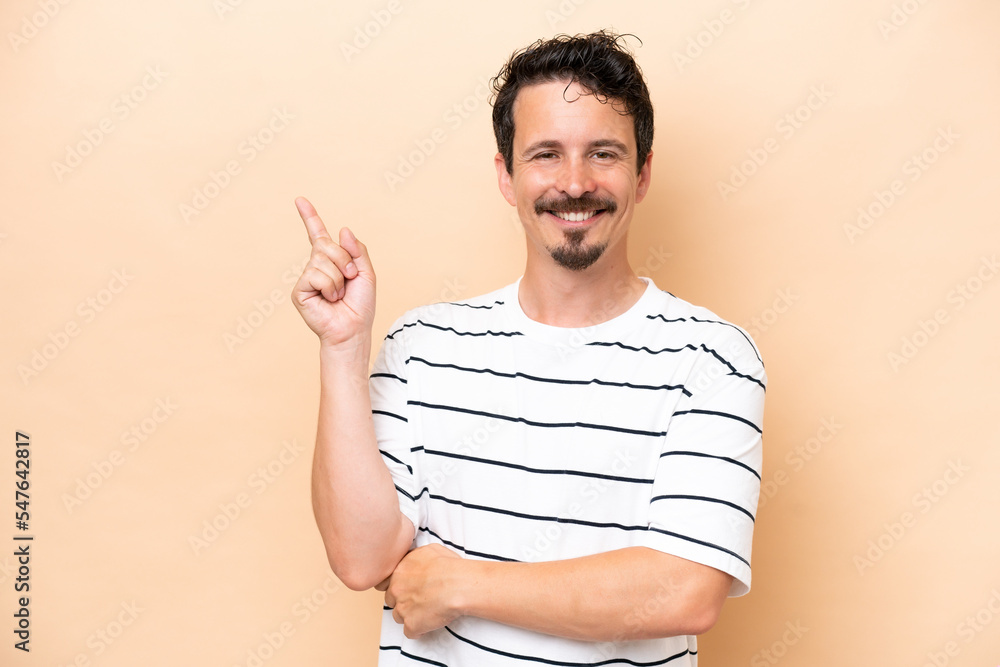 Young caucasian man isolated on beige background happy and pointing up Young caucasian man isolated on beige background happy and pointing up