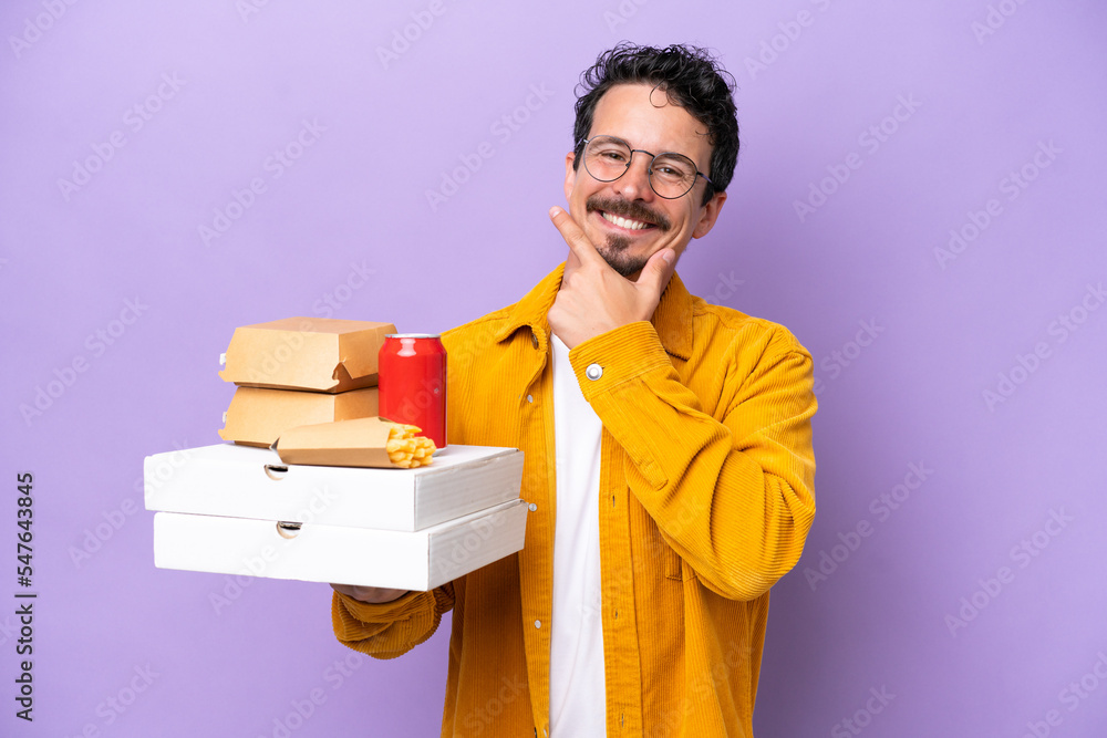 Young caucasian man holding fast food isolated on purple background happy and smiling Young caucasian man holding fast food isolated on purple background happy and smiling